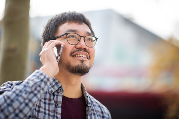Asian man talking on phone in urban setting with blurred background