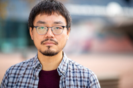 Portrait of an Asian man with neutral expression wearing glasses outdoors