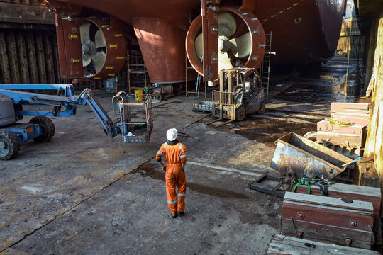 Male worker standing at the bottom of the dry dock, with ship inside, on the blocks. - Powered by Adobe
