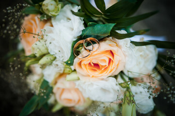 Elegant wedding bouquet featuring soft peach roses with golden wedding rings intertwined