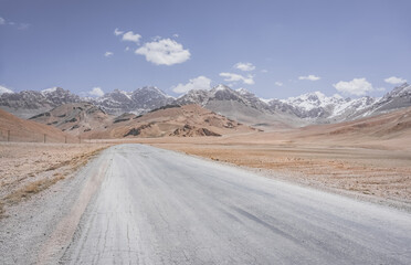 Asphalt road of the Pamir Highway in the valley of the Tien Shan Mountains in Tajikistan in the Pamirs, landscape in the high desert mountains for background, the road goes into the distance