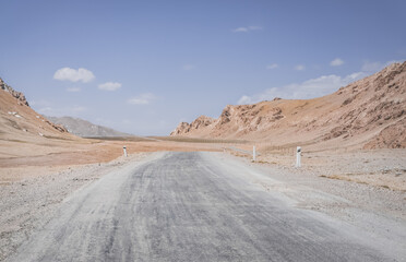 Asphalt road of the Pamir Highway in the valley of the Tien Shan Mountains in Tajikistan in the Pamirs, landscape in the high desert mountains for background, the road goes into the distance