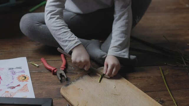 Child engaged in hands-on crafting activity with tools and natural materials indoors during afternoon
