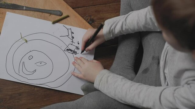 Child creates a colorful drawing while sitting on the floor, showcasing creativity and imagination in an indoor setting during daylight hours