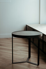 A modern, minimalist black round side table with a metal frame standing on light wooden flooring; coffeeshop layout black table