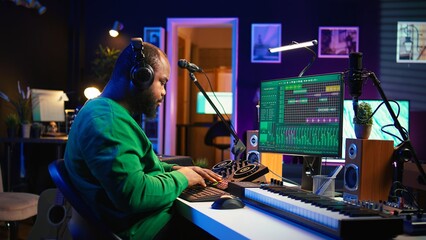 Confident music engineer working on mixing console in home studio, producing new sounds for a song and editing volume levels in daw software. Audio technician recording acoustic files. Camera B.