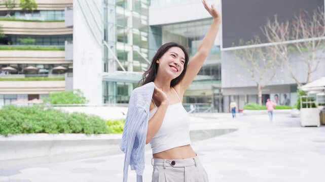 happy young asian woman wave hand in the urban sunny city plaza