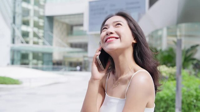 happy young asian woman talking on the phone in the sunny city plaza
