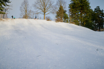 Fun snowy mountain in weekend for families and kids enjoying sleighing on beautiful sunny day in Ikskile, Latvia