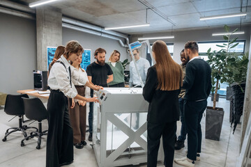 Group of people are standing around the 3d printer in office
