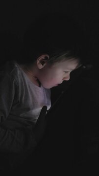 Boy using a tablet in a dark room while focused on content, showing concentration and curiosity at nighttime