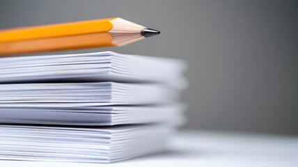 Pencil lies atop stack of white paper sheets