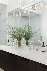 A bathroom detail with a dark wood floating cabinet, decorations on the white marble cabinet, and gold light fixtures mounted on the mirror.