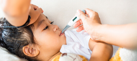 Sick kid. Mother parent checking temperature of her sick daughter with digital thermometer in mouth, child laying in bed taking measuring her temperature for fever and illness, healthcare