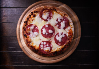 Pizza with salami and mozzarella cheese. Wooden background. Soft focus. Top view. Copy space.