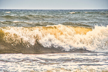 Sea waves rolling on a sandy beach. Close-up of the ocean near the coast. Background on the theme of tourism and family vacation by the water.