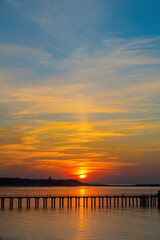 Obraz premium Calm ocean at sunset. Bright orange sun setting in the late evening. Dark silhouette of the port and port cranes.