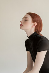 Obraz premium Graceful woman with red hair in a black turtleneck, eyes closed in a serene pose against a soft neutral background.