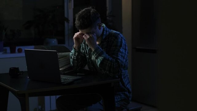 Camera shooting of likable tired overworked man which sleeping on the desk in workroom with night lightings. Boring tired young student or freelancer falling asleep during study or work at home 