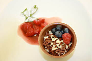 Chocolate mousse in edible chocolate pot with shaved white and milk chocolate, berries and fruit coulis on a white plate