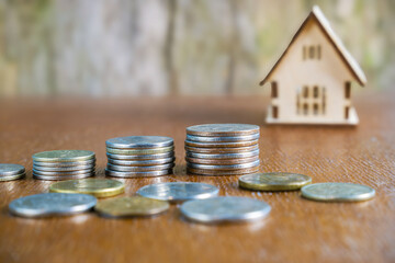 Coins stack and house model on wood table with nature background.