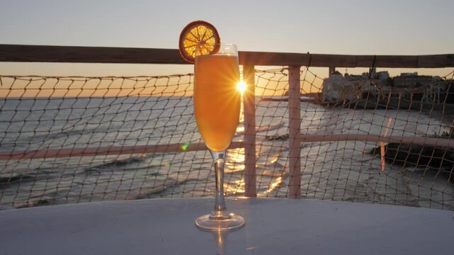 Glass of orange Bellini cocktail on the table in seaside bar restaurant during golden hour. Romantic sunset date at cafe in historic European town Sitges