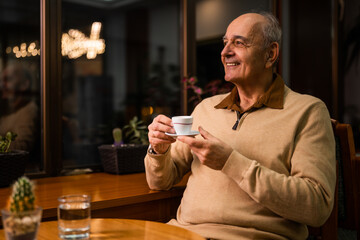 Smiling senior man enjoying sitting in the cozy cafe and drinking coffee at evening.	
