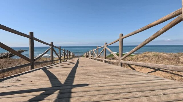 Ground level view walking along wooden path towards the beach with an ocean horizon in the Artola Dunes Natural Park, next to the Mediterranean Sea, in Cabopino of Marbella (Malaga, Andalusia, Spain, 