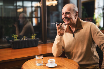 Happy senior man talking on the mobile phone and drinking coffee while sitting in cozy city bar.	