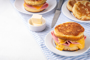 Breakfast crumpet sandwich, british pancake scones burger with cheese and ham, on kitchen table, with stack of crumpets and butter
