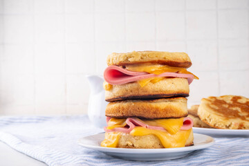 Breakfast crumpet sandwich, british pancake scones burger with cheese and ham, on kitchen table, with stack of crumpets and butter