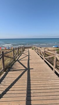 Vertical shot walking along a wooden path towards the beach with the Mediterranean Sea horizon in the Artola Dunes Natural Park, in Cabopino of Marbella (Malaga, Andalusia, Spain, Europe)
