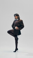 Beautiful young woman wears heels, oversized brown blazer with tie and black tights, posing with...