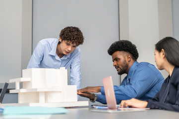 Architects engineers collaborating on building design project in modern office, diverse team of professionals female muslim architect and male engineers discussing architectural model of structure