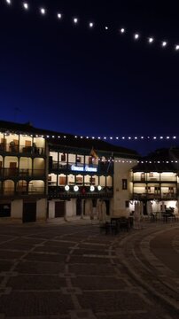 Vertical video of a large tree of lights illuminated in the famous town square of Chinchon at night at Christmas, with traditional buildings and people celebrating, in Madrid, Spain
