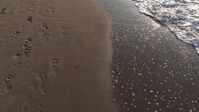 Walking along the shore of a brown sand beach where the waves of the sea arrive