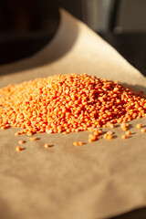 A pile of orange lentils sits on a brown surface, bathed in sunlight.  A simple, natural food image.
