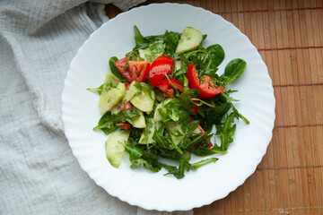Fresh salad with tomatoes, cucumbers, and arugula on a white plate. A healthy and delicious meal.