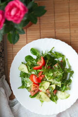 Fresh salad with tomatoes, cucumbers, and arugula on a white plate.