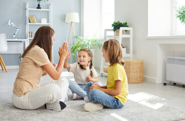 Young smiling mother giving high five with children sitting on floor at home on weekend. Happy family spending time indoors playing in the living room. Family leisure and mothers day concept.