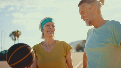 Beautiful happy senior couple playing basketball and having fun - Mature married couple in love bonding outdoors and doing sport together, concepts about elderly lifestyle and relationship - Powered by Adobe