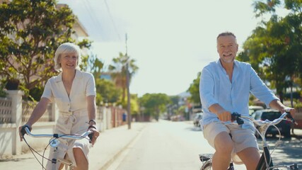Beautiful happy senior couple dating at the seaside during summertime - Mature married couple in love bonding outdoors and riding bicycle, concepts about elderly lifestyle, transportation and quality - Powered by Adobe