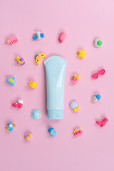 A flat lay of pastel blue lotion tubes on a pink background. Surrounding with colorful plastic toys, flowers, and other playful items
