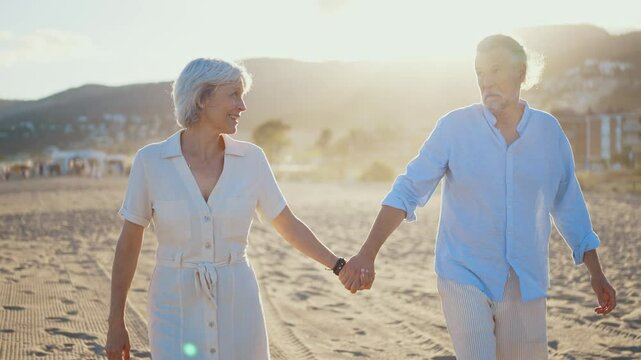 Beautiful happy senior couple dating at the seaside during summertime - Mature married couple in love bonding outdoors at the beach, concepts about elderly lifestyle, relationship and quality of life
