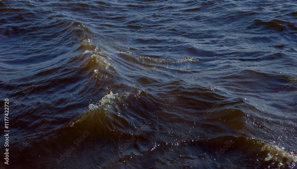 Poster close-up view of gentle brownish waves with sparkling droplets on windy water surface, capturing nat