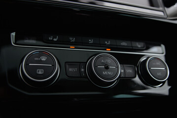 Modern car climate control panel with buttons and dials for temperature fan speed and AC