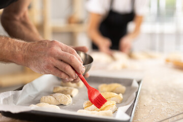 Baker's hands grease pieces of dough on baking sheet