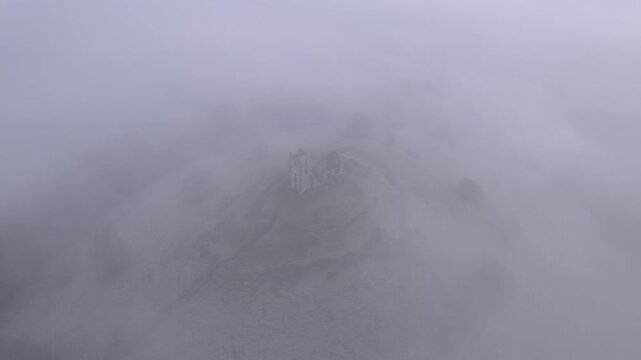 Aerial drone scene of Burrow Mump at Sunrise with dense Inversion Fog in England