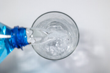 Overhead shot of blue bottle refilling glass with mineral water. Concept: Glass, water, restoration.