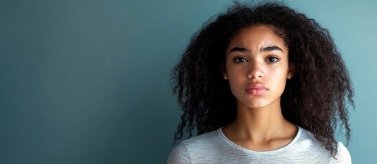Upset Diverse Teenage Girl with Curly Hair Against Calm Blue Background with Ample Copyspace for Text and Emotional Expression